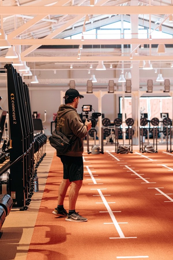 Jan Castany grabando con una cámara de cine en un gimnasio con pista de atletismo.