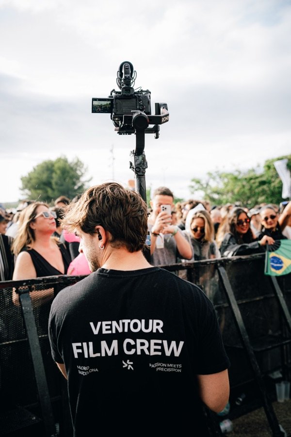 Jan Castany de espaldas frente al público de un festival, con una cámara sobre gimbal y una camiseta del equipo de rodaje.